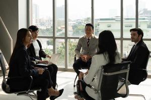 équipe commerciale internationale comprenant des personnes caucasiennes et asiatiques debout près de la fenêtre du bureau et discutant du projet. diversité dans le concept d'entreprise photo