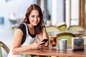 femme aux yeux bleus assise sur un café urbain à l'aide d'un téléphone intelligent photo