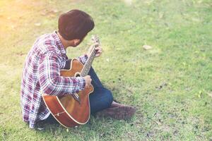 jeune homme hipster a pratiqué la guitare dans le parc, heureux et aime jouer de la guitare. photo