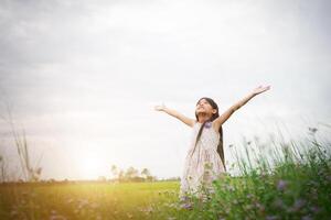 petite fille asiatique mignonne debout parmi le jour de soleil de champ de fleurs pourpres. la liberté de profiter de la nature. photo