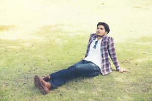 jeune homme hipster assis sur l'herbe dans le parc, profitez de l'air frais et naturel de la brise. photo