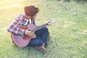 jeune homme hipster a pratiqué la guitare dans le parc, heureux et aime jouer de la guitare. photo