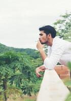 jeune homme hipster prenant du repos, fumant une cigarette avec la nature et la brise fraîche. photo