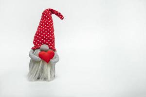 nain dans un chapeau rouge avec un coeur rouge dans ses mains isolé sur fond blanc. idée saint valentin photo