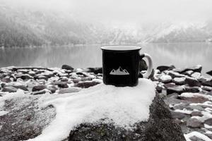 tasse pour l'inscription. tasse noire sur le fond d'un lac de montagne en hiver photo