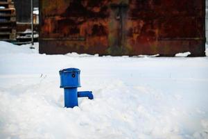 distributeur d'eau bleu sur neige haute près d'un garage en métal rouillé avec cadenas photo