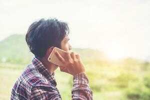 jeune homme barbu hipster parlant au téléphone, souriant, à l'extérieur de la vue sur la montagne. photo