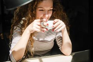 heureuse jeune femme caucasienne buvant du café tout en regardant une vidéo sur un ordinateur portable à la maison photo