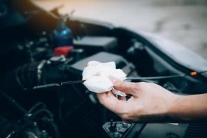 le mécanicien automobile vérifie l'huile moteur de la voiture à l'aide d'un acier et d'un nettoyant par tissu. photo