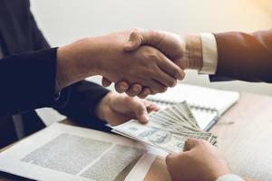 deux hommes d'affaires se serrant la main tandis qu'un homme donne de l'argent et reçoit de l'argent sale dans la salle de bureau avec le concept de corruption. photo