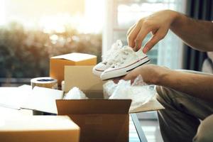 un adolescent entrepreneur asiatique porte des chaussures de bébé et met dans une boîte en carton un client pour livrer le produit à la maison. photo