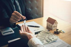 les agents immobiliers distribuent les clés aux acheteurs de maisons qui signent des contrats au bureau. photo