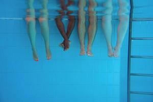 jambes d'un homme afro-américain avec des amis caucasiens dans la piscine sous l'eau. été. concept de vacances, international et sportif. photo