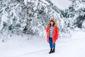 femme dans une veste chaude rouge et un chapeau sur fond de forêt enneigée photo