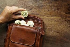 la main de l'homme ramasse les bitcoins, l'argent est contenu dans des sacs en cuir marron sur un bureau en bois très brillant. concept de design pour les affaires et le commerce photo