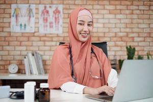 portrait d'une belle femme médecin, belle musulmane en uniforme avec un stéthoscope, souriante et travaillant avec un ordinateur portable dans la clinique de l'hôpital. une personne qui a une expertise dans le traitement professionnel. photo