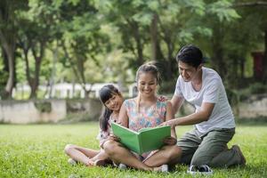 mère de famille heureuse, père et fille lisent un livre dans le parc photo