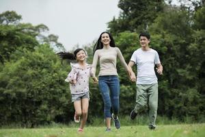 une famille heureuse s'amuse mère, père et fille courent dans le parc. photo