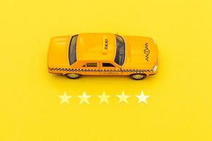 taxi voiture jouet jaune et cote 5 étoiles isolé sur fond jaune. application smartphone du service de taxi pour la recherche en ligne, appeler et réserver le concept de taxi. symbole de taxi. espace de copie. photo