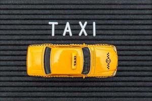 concevez simplement le modèle de taxi de voiture de jouet jaune avec le mot de lettres de taxi d'inscription sur le fond noir. symbole de l'automobile et du transport. concept d'idée de service urbain de livraison de trafic urbain. espace de copie. photo
