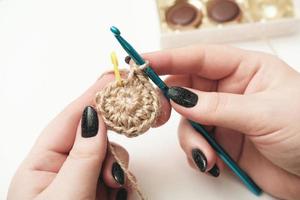 mains d'une femme tenant du fil de crochet et de jute et un fragment d'un motif tricoté. tricot écologique naturel, dessous de tasse fait à la main. artisanat et passe-temps. décor à la maison écologique photo