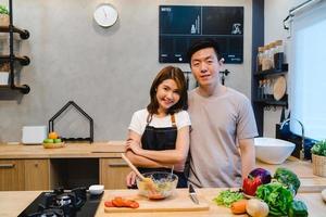 couple asiatique prépare la nourriture ensemble. bel homme et femme asiatique heureux cuisinent dans la cuisine. un jeune couple asiatique passe un moment romantique tout en restant à la maison. mode de vie de couple à la maison concept. photo