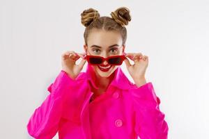 gros plan de visage de femme heureux, choc, excité. fille en vêtements d'automne rose vif, lunettes de soleil rouges isolées sur fond blanc, espace de copie. belle femelle surprise, gaie. amusement drôle modèle crier photo