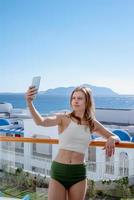 femme heureuse en maillot de bain prenant selfie debout sur le balcon de la chambre d'hôtel photo