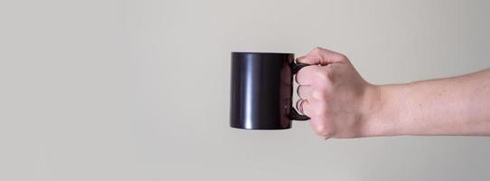 mug noir entre les mains d'un homme sur fond clair. photo