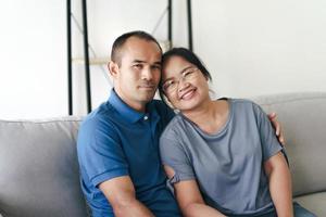 portrait d'un couple mature asiatique assis dans le salon. femme et mari s'embrassant, tenant la main avec bonheur et gaieté. concept de famille d'amour, de sécurité et d'assurance photo