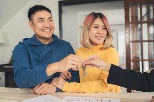 heureux jeune couple asiatique et agent immobilier. joyeux jeune homme signant certains documents et poignée de main avec un courtier alors qu'il était assis au bureau. signature du contrat de bon état. photo