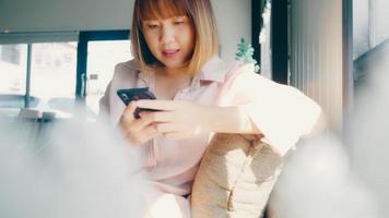 femme asiatique indépendante d'affaires utilisant un smartphone pour parler, lire et envoyer des SMS tout en étant assise sur une table dans un café. mode de vie intelligent belles femmes travaillant au concept de café. photo