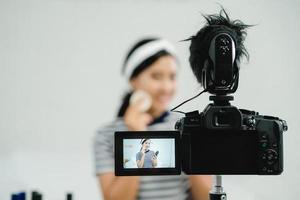 un blogueur de beauté présente un cosmétique de beauté tout en étant assis devant la caméra pour enregistrer une vidéo. belle femme utilise du rouge à lèvres pendant la révision du didacticiel de maquillage diffusé une vidéo en direct sur le réseau social par internet. photo