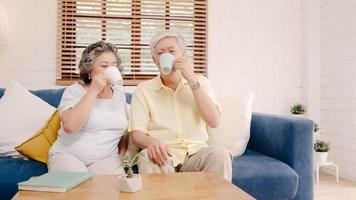 couple âgé asiatique buvant du café chaud et parlant ensemble dans le salon à la maison, couple profitant d'un moment d'amour allongé sur un canapé lorsqu'il est détendu à la maison. concept de famille senior de style de vie à la maison. photo