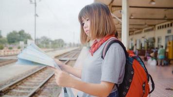 femme asiatique voyageuse direction et regardant sur la carte de localisation tout en passant des vacances et en attendant le train à la gare, jeune femme routard touristique profiter du voyage. concept de voyage de femmes de style de vie photo