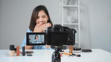 Heureuse femme asiatique souriante ou blogueuse beauté avec brosse et caméra d'enregistrement vidéo et agitant la main à la maison. beauté videoblog blogging personnes concept. photo