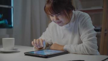 jeune femme asiatique travaillant tard à l'aide d'une tablette vérifiant les médias sociaux tout en vous relaxant sur le bureau la nuit dans le salon à la maison. profiter du concept de temps à la maison. photo