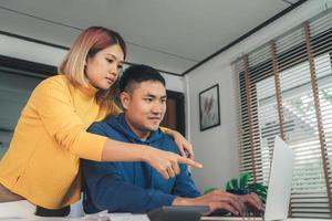 jeune couple asiatique gérant les finances, examinant leurs comptes bancaires à l'aide d'un ordinateur portable et d'une calculatrice dans une maison moderne. femme et homme faisant de la paperasse ensemble, payant des impôts en ligne sur un ordinateur portable.