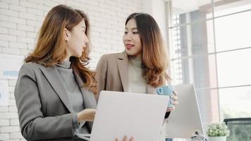 deux jeunes femmes d'affaires créatives asiatiques tenant une tasse de café, travaillant sur un ordinateur portable et discutant du travail tout en travaillant au bureau. affaires occasionnelles, travail indépendant au café, concept de réunion sociale. photo