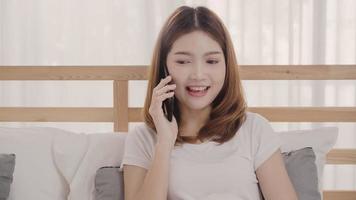 jeune femme asiatique utilisant un smartphone allongée sur son lit après s'être réveillée le matin, belle jolie fille japonaise souriante se détendre dans la chambre à la maison. profiter du temps de vie des femmes à la maison. photo