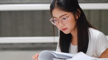 étudiantes asiatiques lisant des livres dans la bibliothèque de l'université. une jeune fille de premier cycle fait ses devoirs, lit des manuels, étudie dur pour acquérir des connaissances et de l'éducation sur un pupitre de conférence sur le campus universitaire. photo