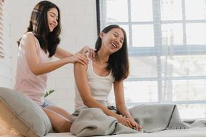 un couple de femmes lgbtq lesbiennes asiatiques se massent à la maison. jeune amant d'asie femme heureuse se détendre se reposer après le réveil, bien-être du corps dans la chambre à la maison le matin concept. photo