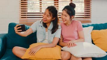 jeune couple de femmes lgbtq lesbiennes selfie à la maison. amant asiatique femme heureuse se détendre s'amuser en utilisant la technologie téléphone mobile souriant prendre une photo ensemble tout en étant allongé sur un canapé dans le concept de salon.