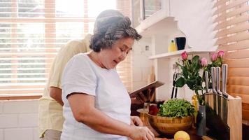 un couple de personnes âgées asiatiques coupe des tomates préparent des ingrédients pour faire de la nourriture dans la cuisine, le couple utilise des légumes biologiques pour une alimentation saine à la maison. mode de vie famille senior faisant de la nourriture à la maison concept. photo