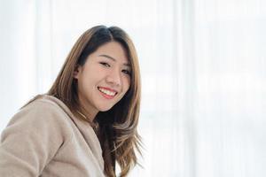 portrait belle jeune femme asiatique sur le lit à la maison le matin. femme asiatique joyeuse portant un pull confortable et souriant sur son lit. salle de détente. mode de vie asie femme à la maison concept. photo