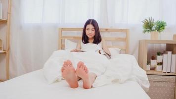 belle jeune femme asiatique séduisante lisant un livre allongée sur le lit lorsqu'elle se détend dans sa chambre à la maison le matin. femmes de style de vie utilisant le concept de temps de détente à la maison. photo