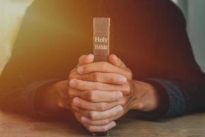 les mains d'un homme priant sur une bible représentent la foi et la spiritualité dans la vie quotidienne. fermer. photo