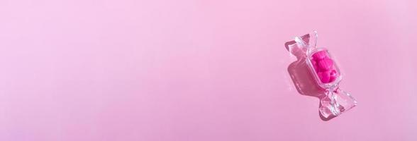 boîte transparente en forme de bonbon avec des sucettes au coeur doux avec une ombre dure sur l'espace de copie de fond rose. le concept de la saint valentin, fête des mères. photo