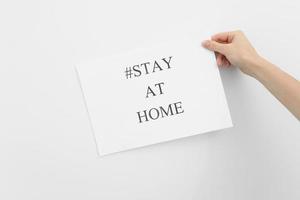 concept de rester à la maison. main de femme tenant du papier avec des mots rester à la maison isolé sur fond blanc. coronavirus, covid-19, auto-quarantaine, isolement photo