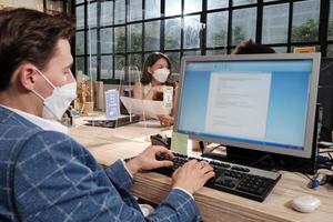 équipe multiraciale de collègues avec masque facial travaillant dans un nouveau bureau normal. protection covid-19 par cloison dégagée, bureau de travail, distanciation sociale pour la santé pandémique, prévention des maladies. photo